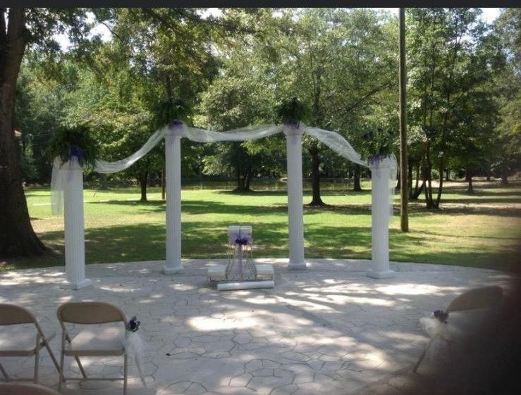 A wedding ceremony in a park with white pillars and chairs