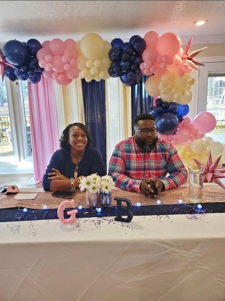 A man and a woman are sitting at a table with balloons in the background.