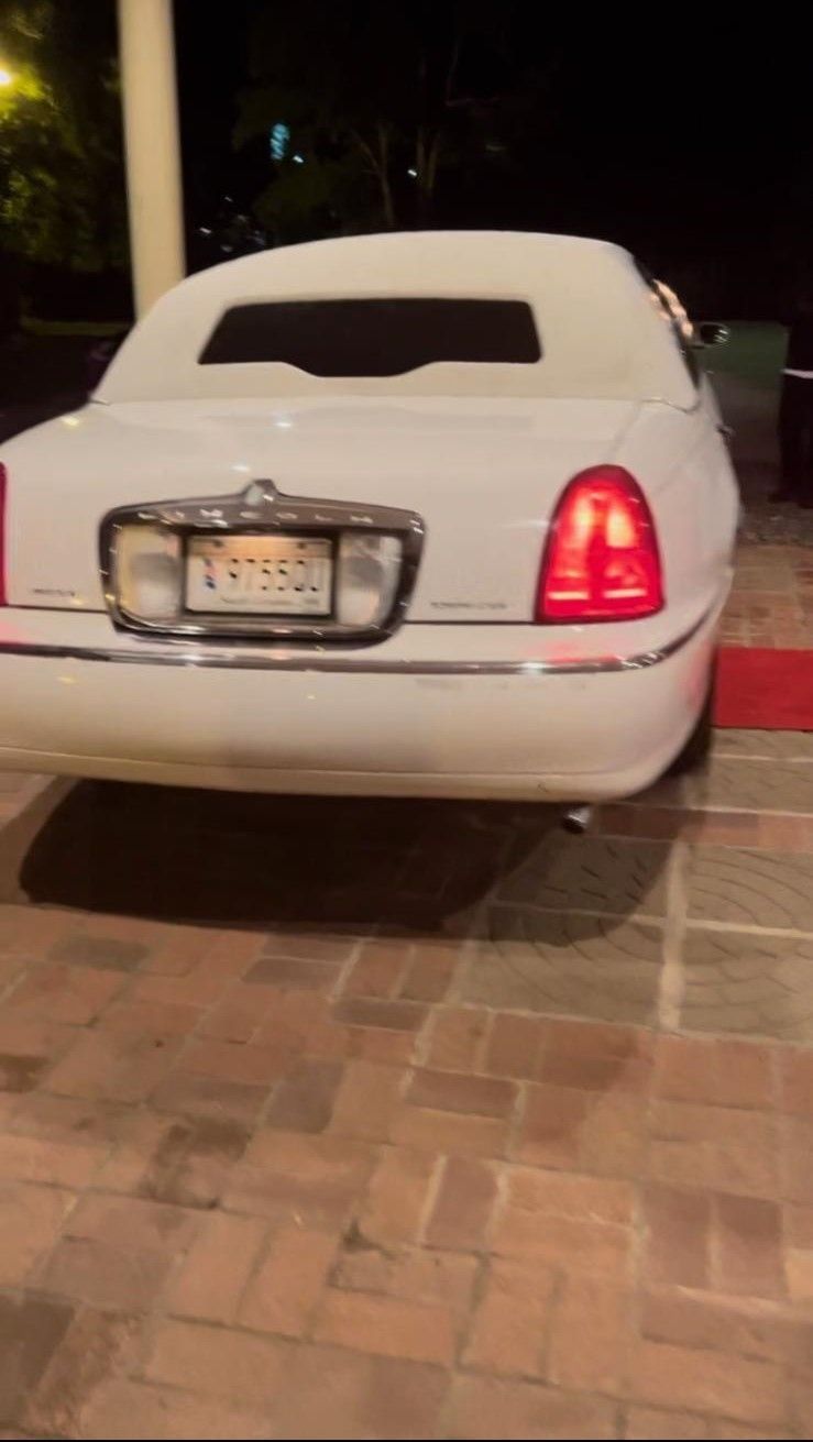 A white limousine is parked on a brick driveway at night.