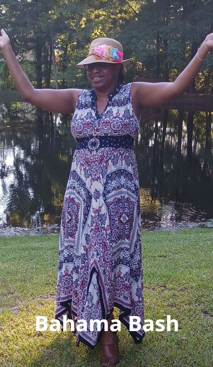 A woman in a dress and hat is standing in the grass with her arms outstretched.