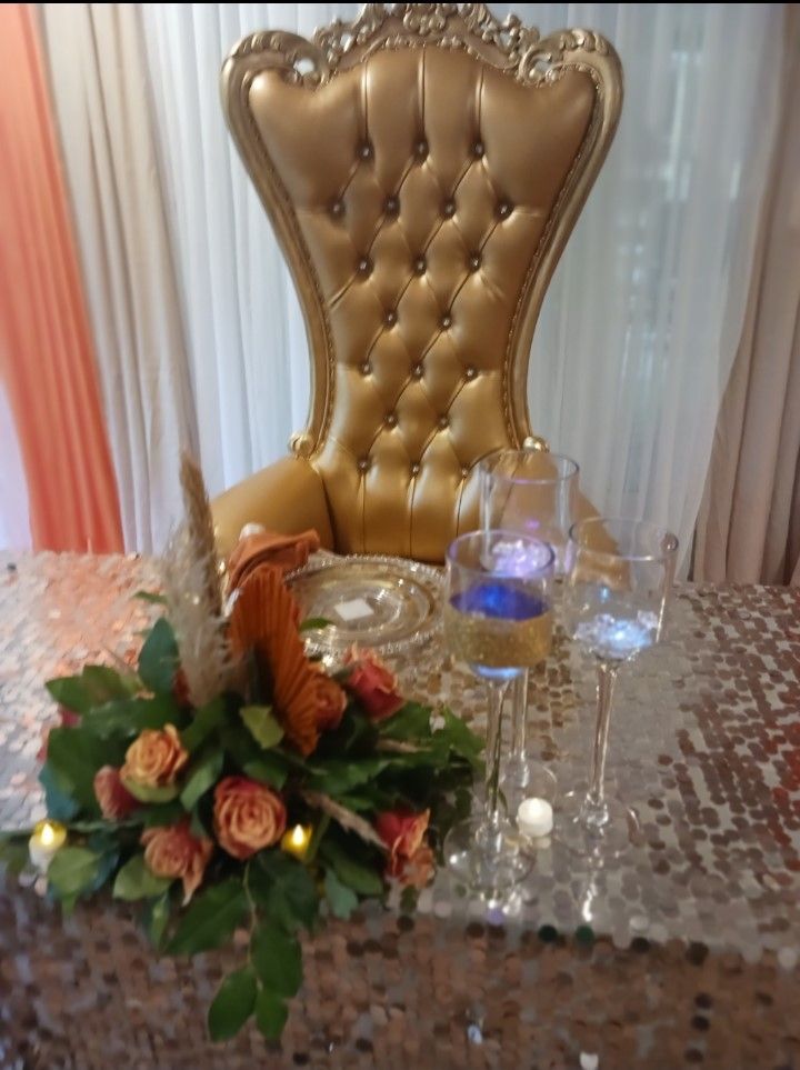 A gold chair is sitting on top of a table with flowers and wine glasses.