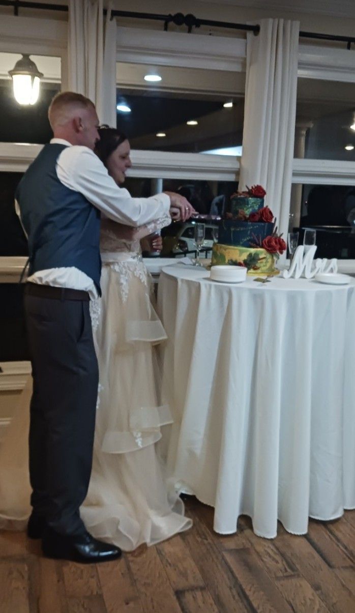 A bride and groom are cutting their wedding cake at a table.