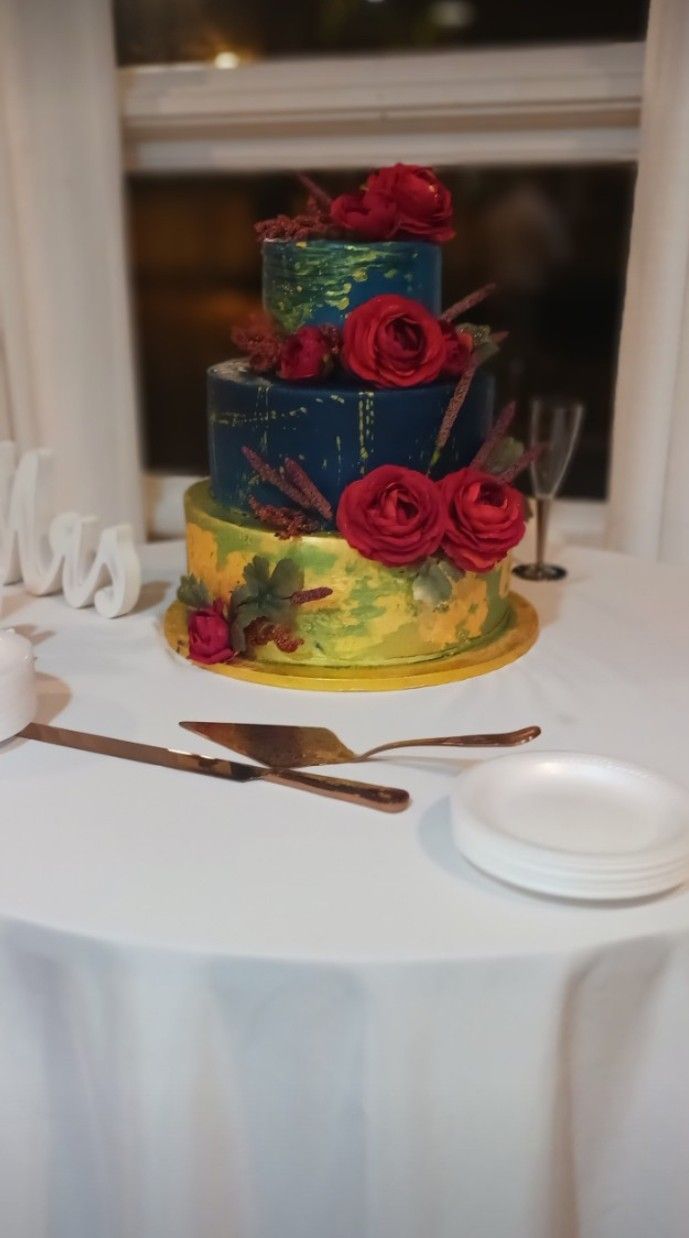 A wedding cake with red roses is sitting on a table.