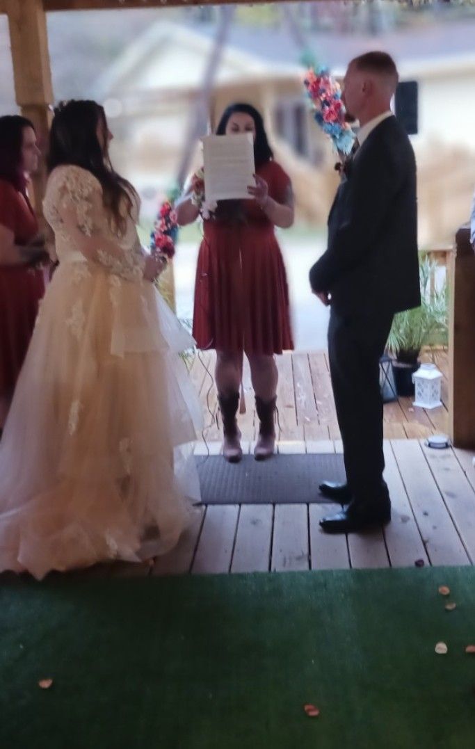 A bride and groom are standing in front of a woman holding a piece of paper.