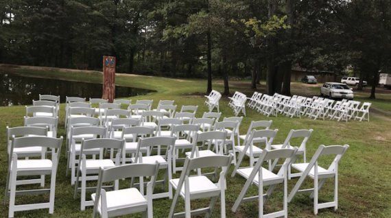A row of white folding chairs sitting on top of a lush green field.