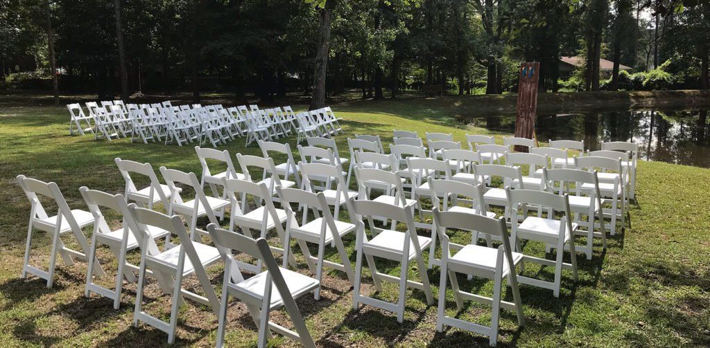 A row of white folding chairs are lined up in a circle in the grass.
