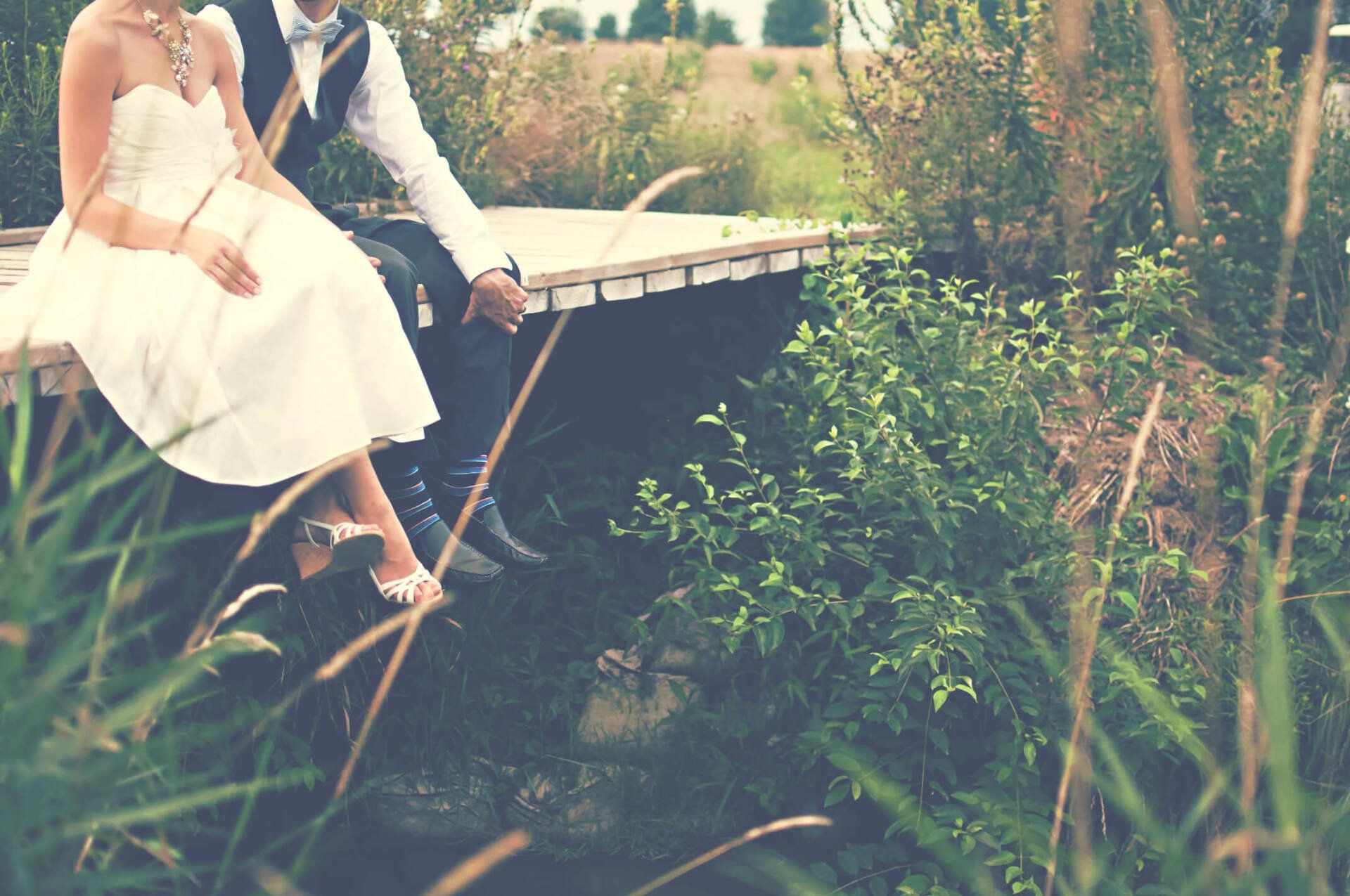 A bride and groom are sitting on a dock holding hands.