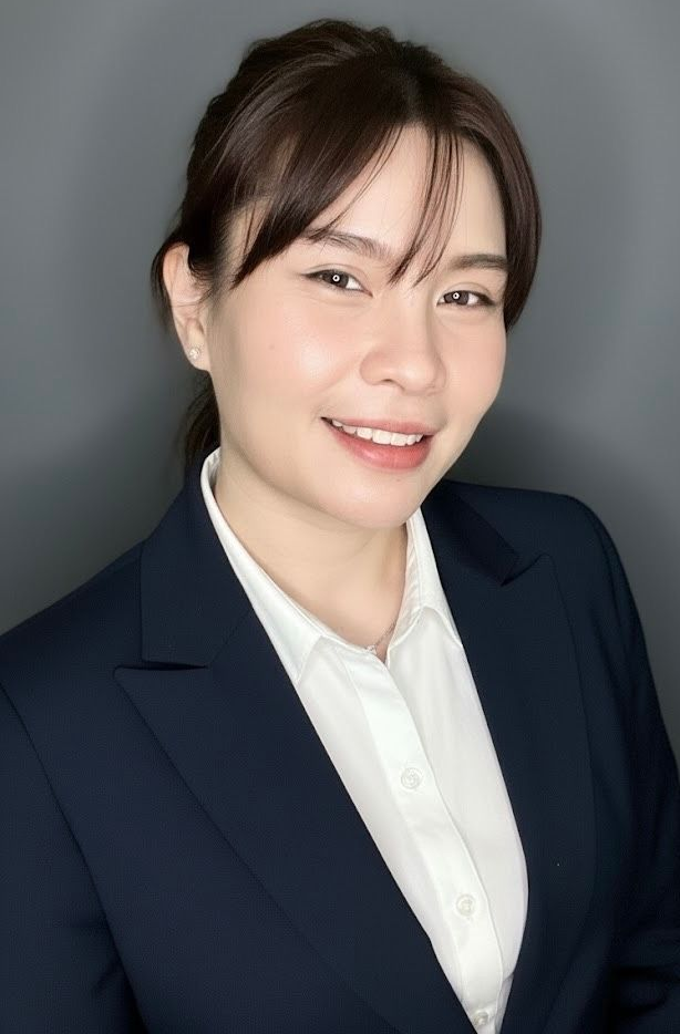 Woman in navy blazer and white shirt smiling at the camera against a gray background.