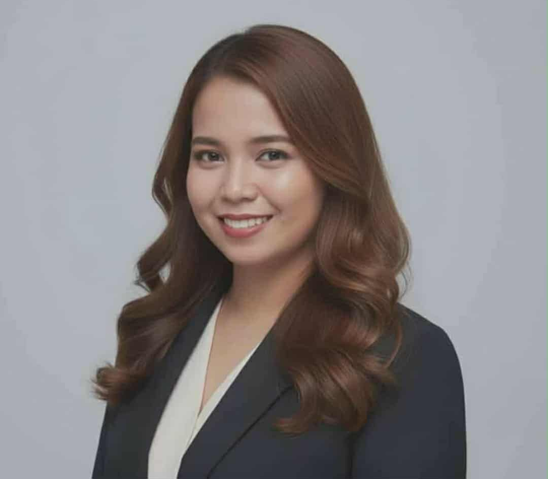 Woman with brown hair smiles, wearing a black blazer and white top, against a gray backdrop.