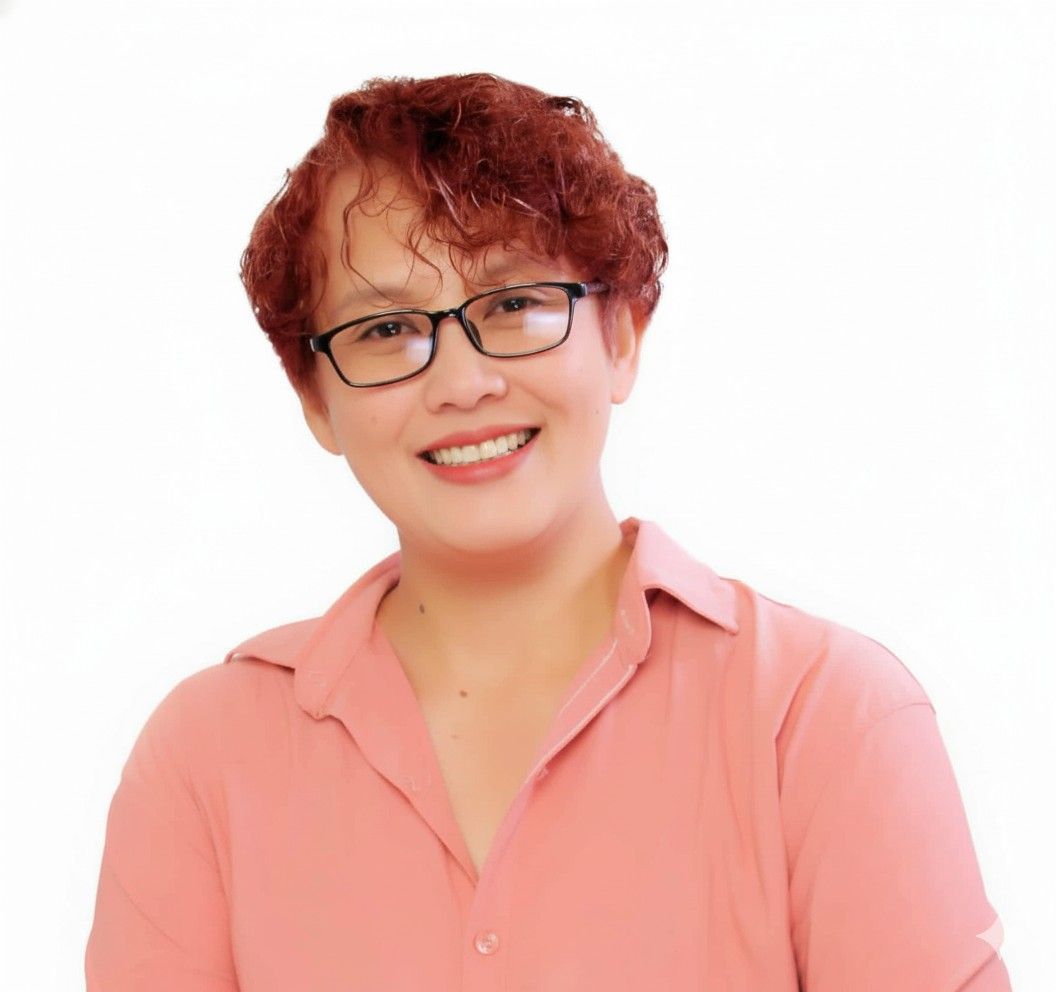 Woman with short curly red hair, glasses, and pink shirt smiling.