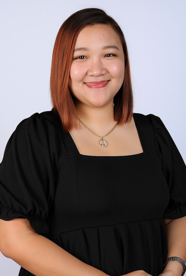 Woman with reddish-brown hair, smiling, wearing a black top and necklace, posing against a white backdrop.