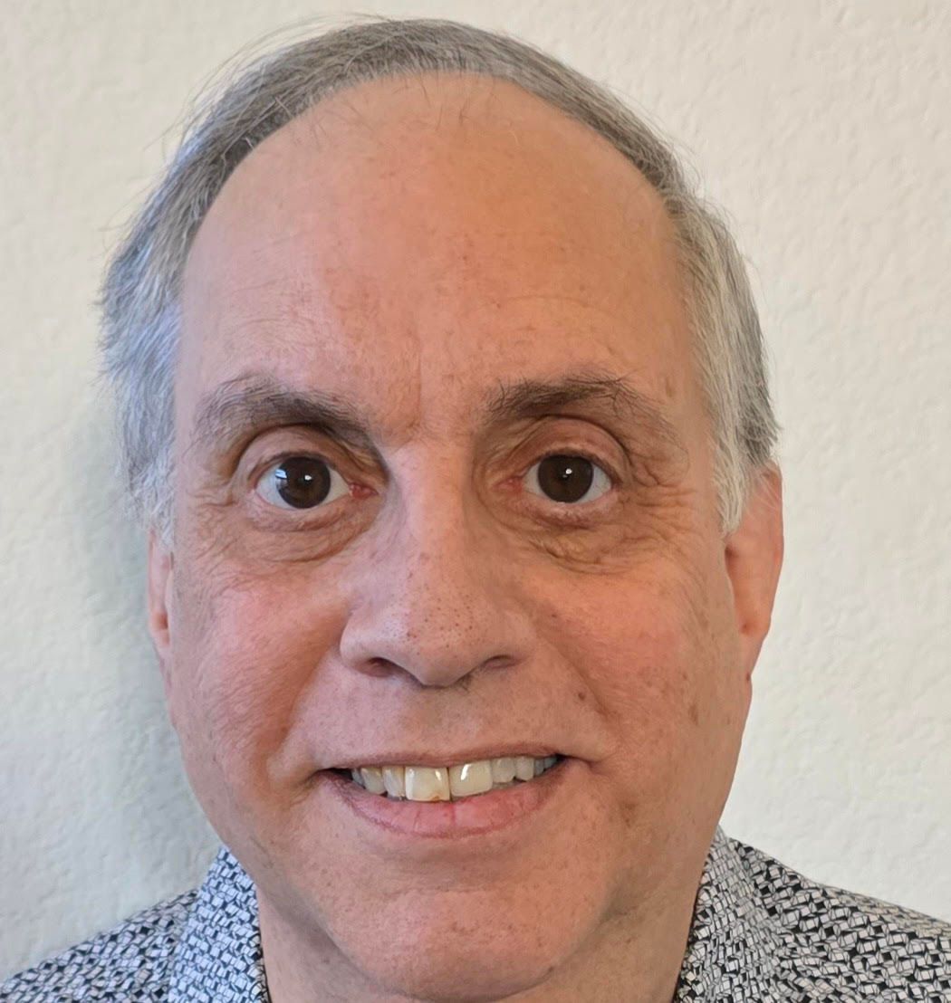 Man with graying hair smiling, wearing a patterned shirt, looking directly at the viewer.