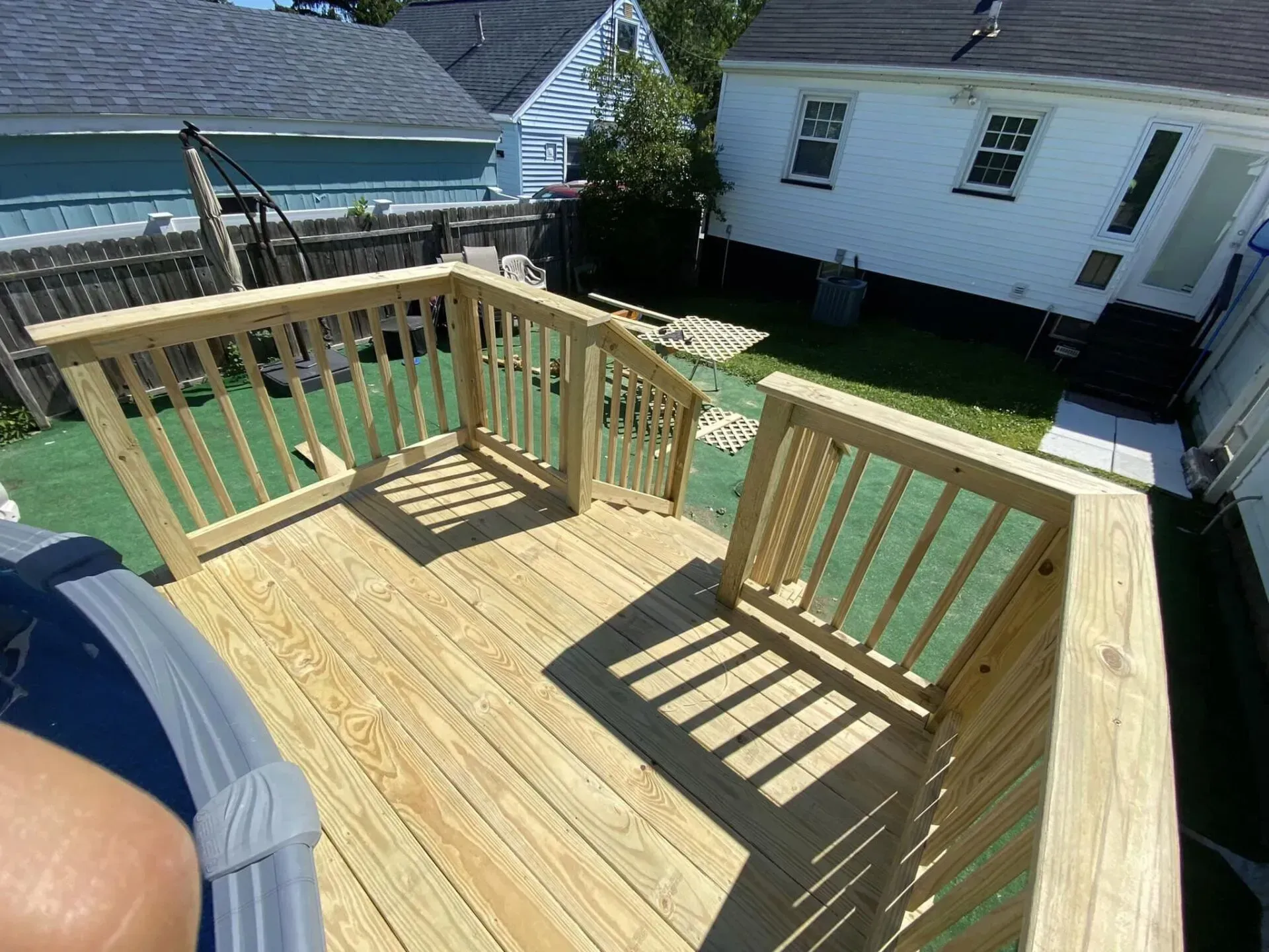 A person is standing on a wooden deck next to a pool.