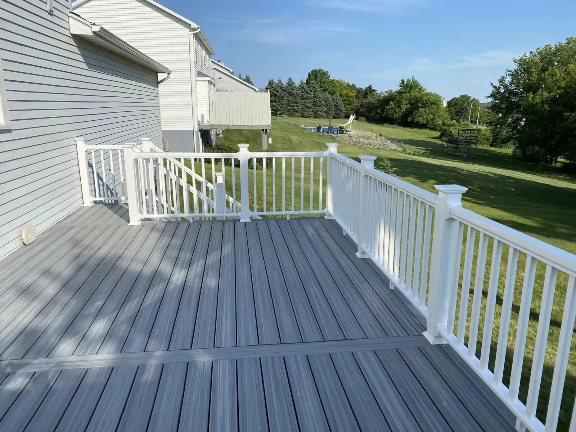 A gray deck with a white railing and a house in the background.