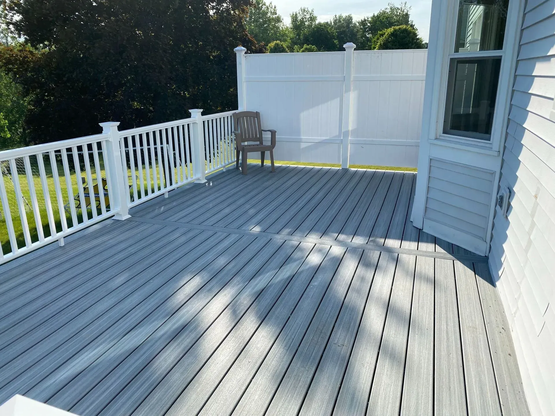 A gray deck with a white railing and a chair on it