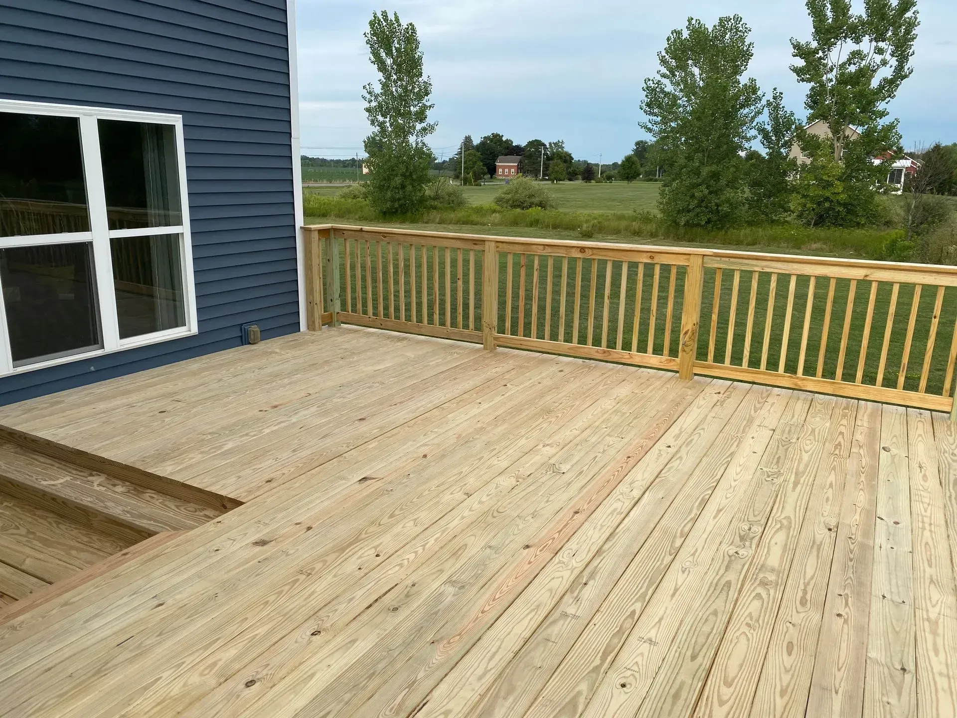 A large wooden deck with a wooden railing is in front of a blue house.