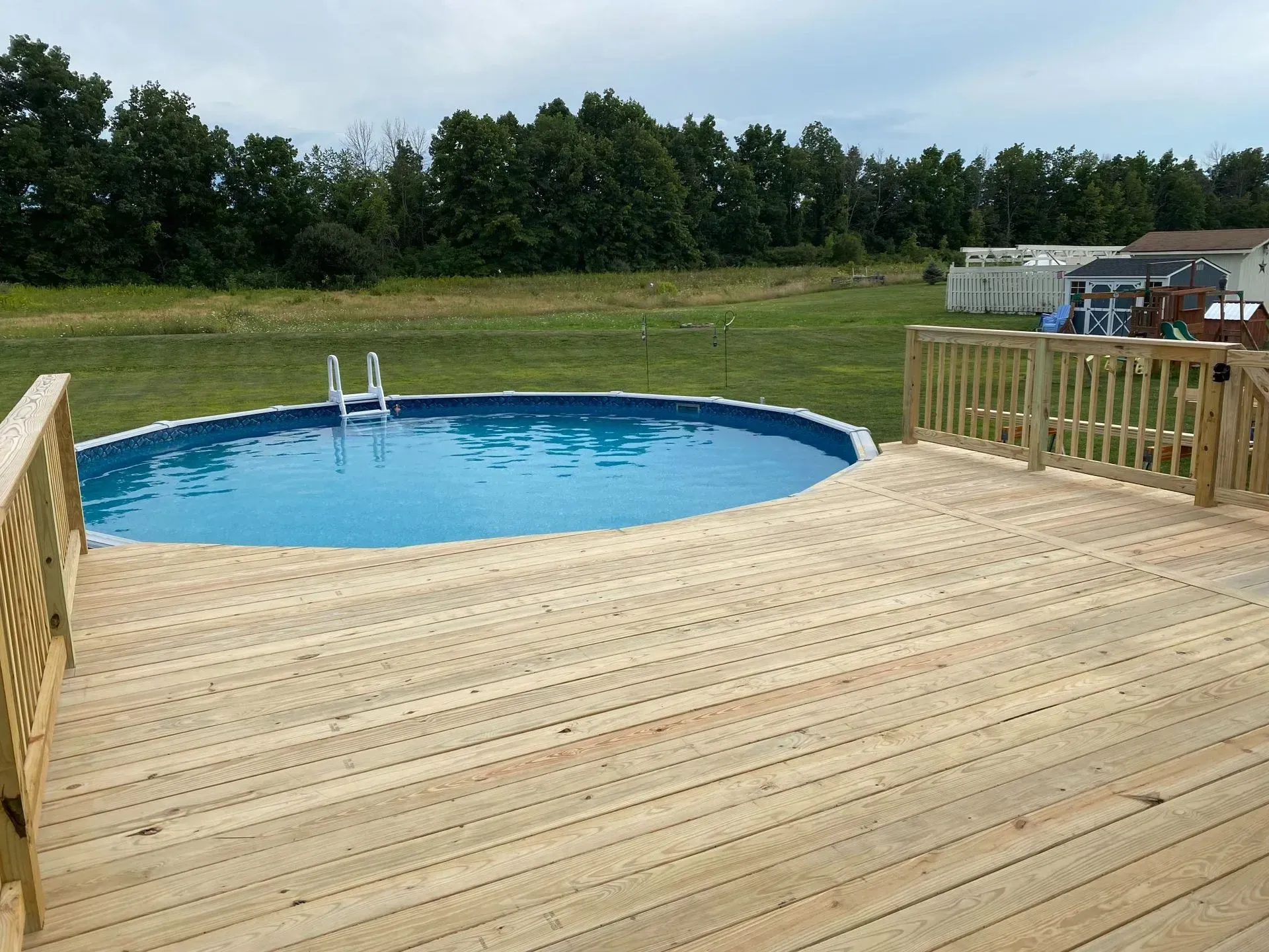 A wooden deck with a swimming pool in the background