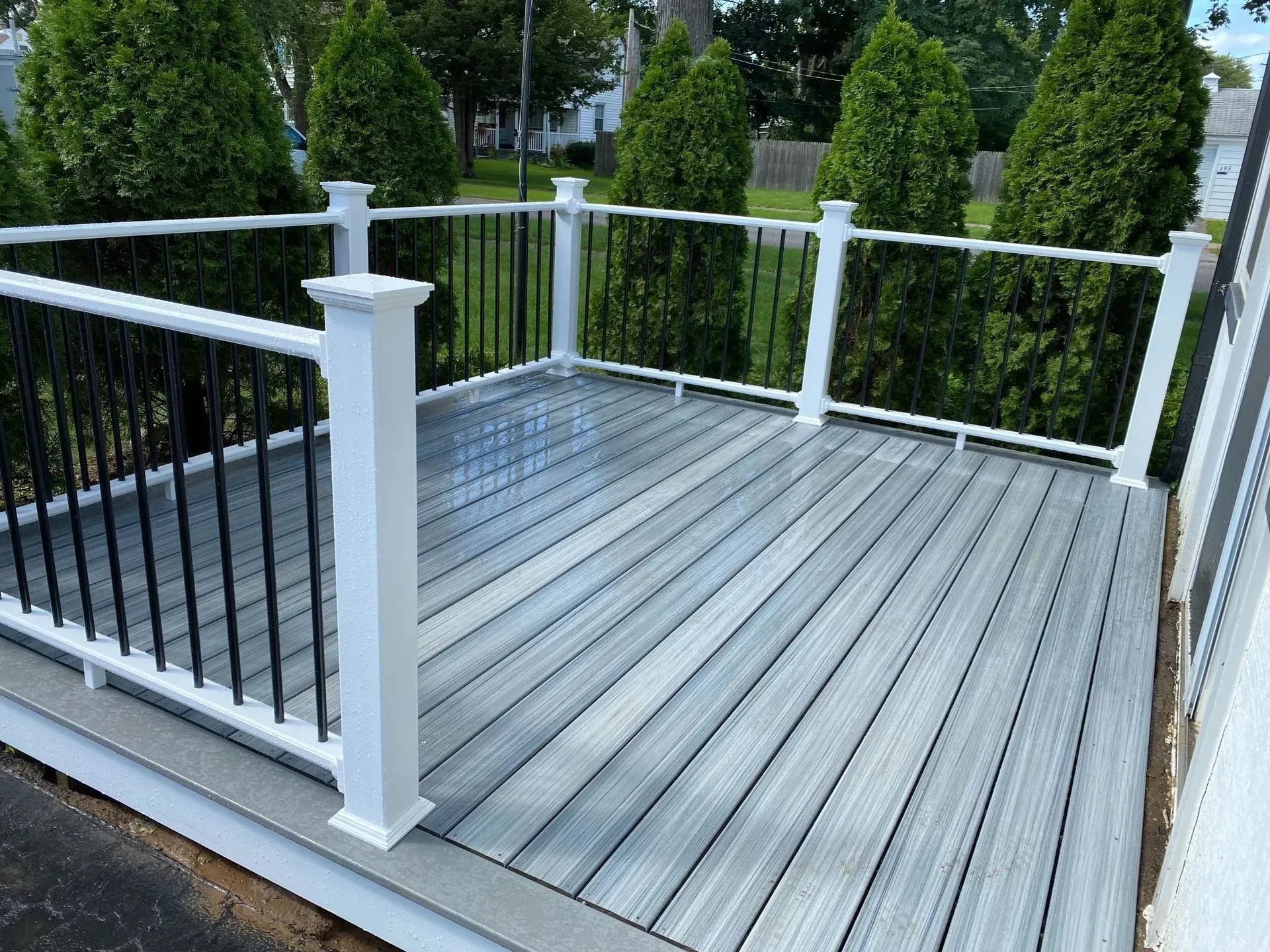 A gray deck with a white railing and trees in the background.