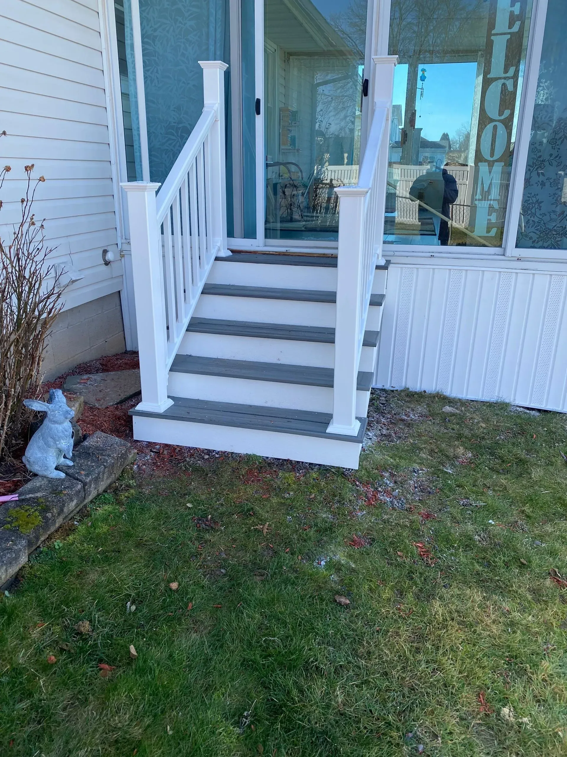 A white porch with stairs leading up to a sliding glass door.