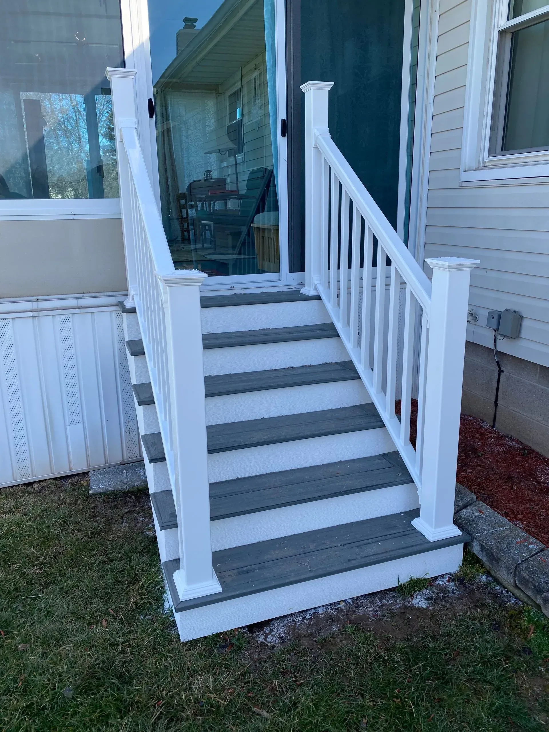 A white deck with stairs leading up to a sliding glass door.