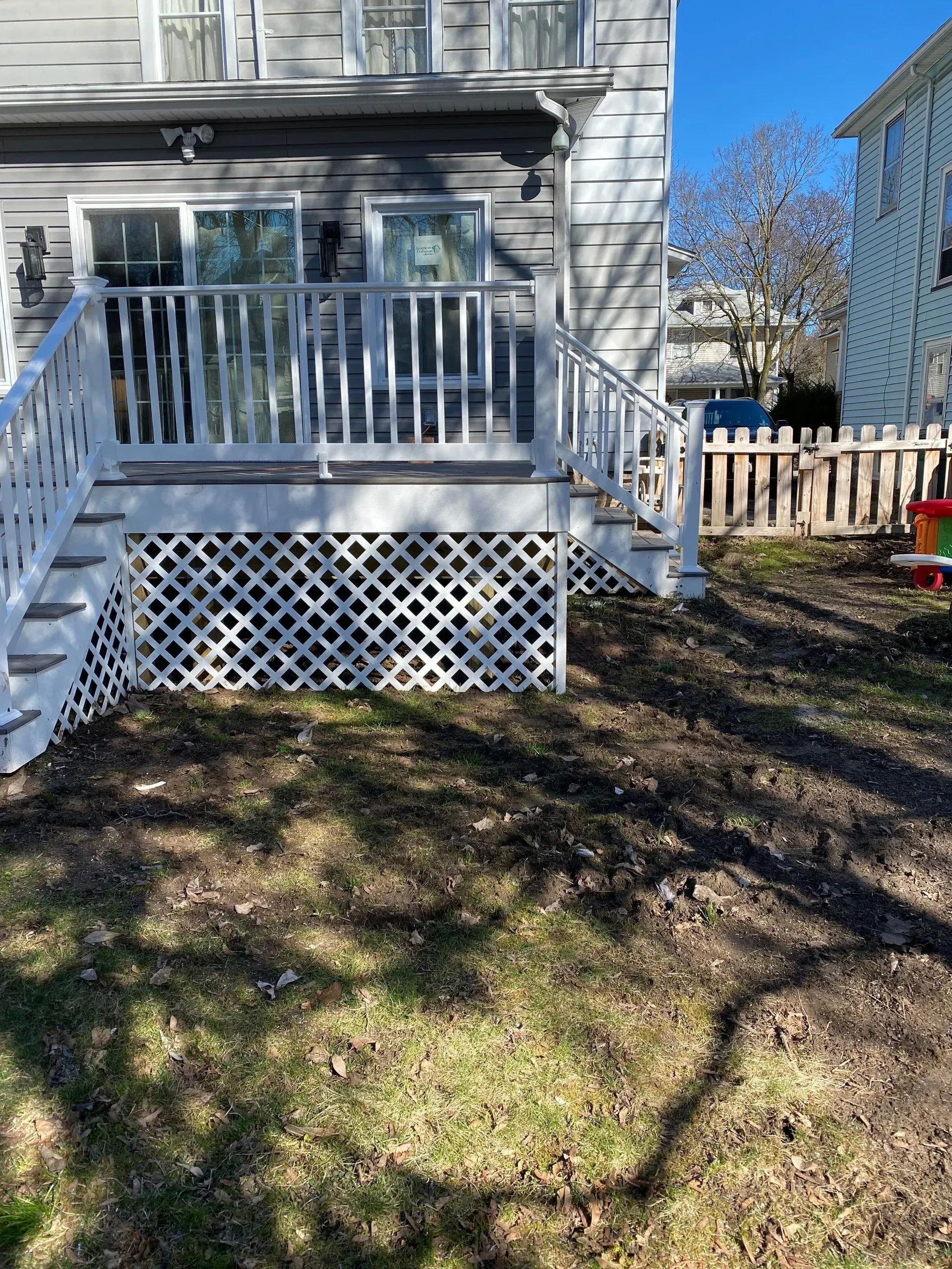 A white deck with stairs leading up to it is in the backyard of a house.