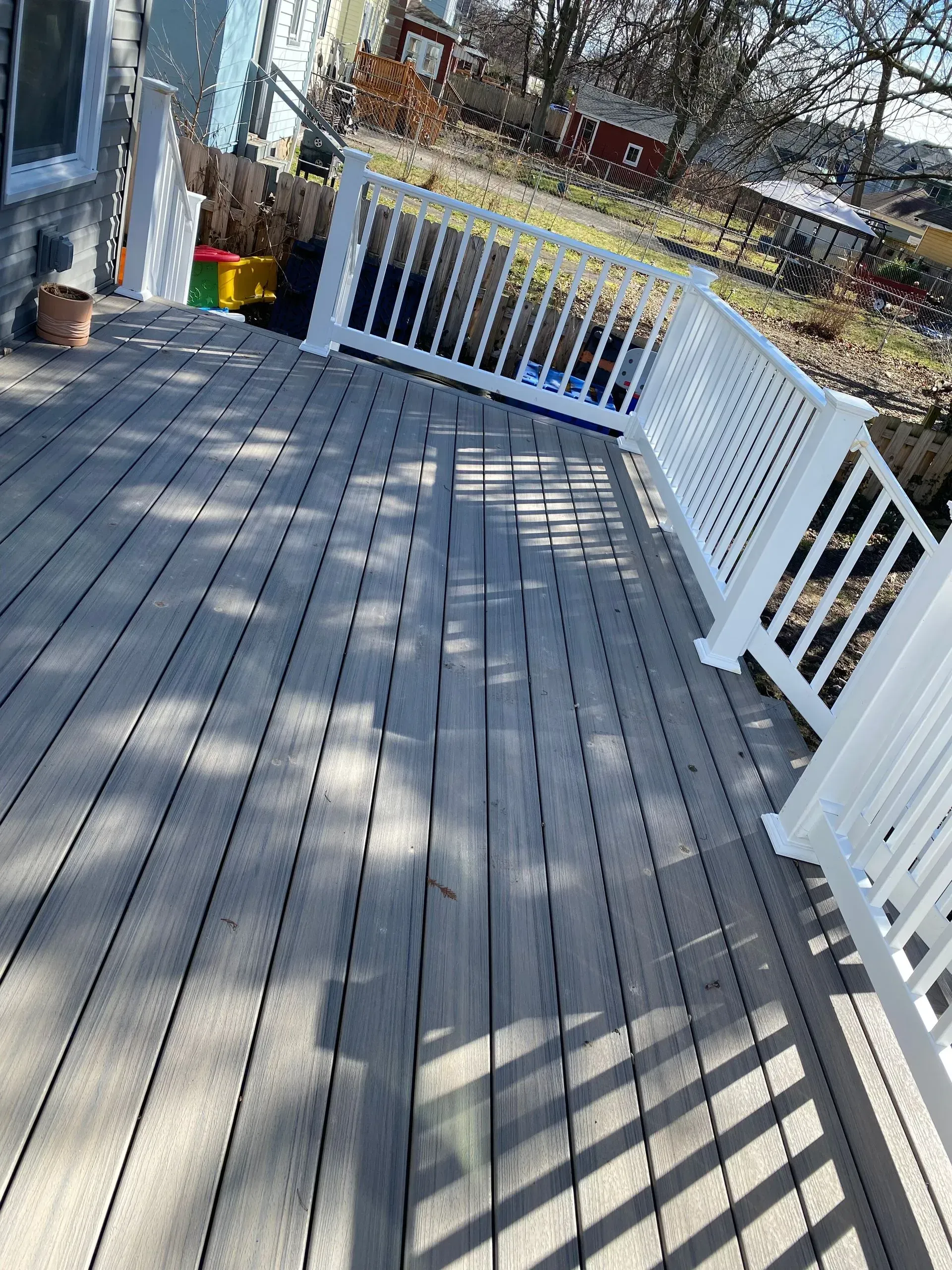 A wooden deck with a white railing and a house in the background.