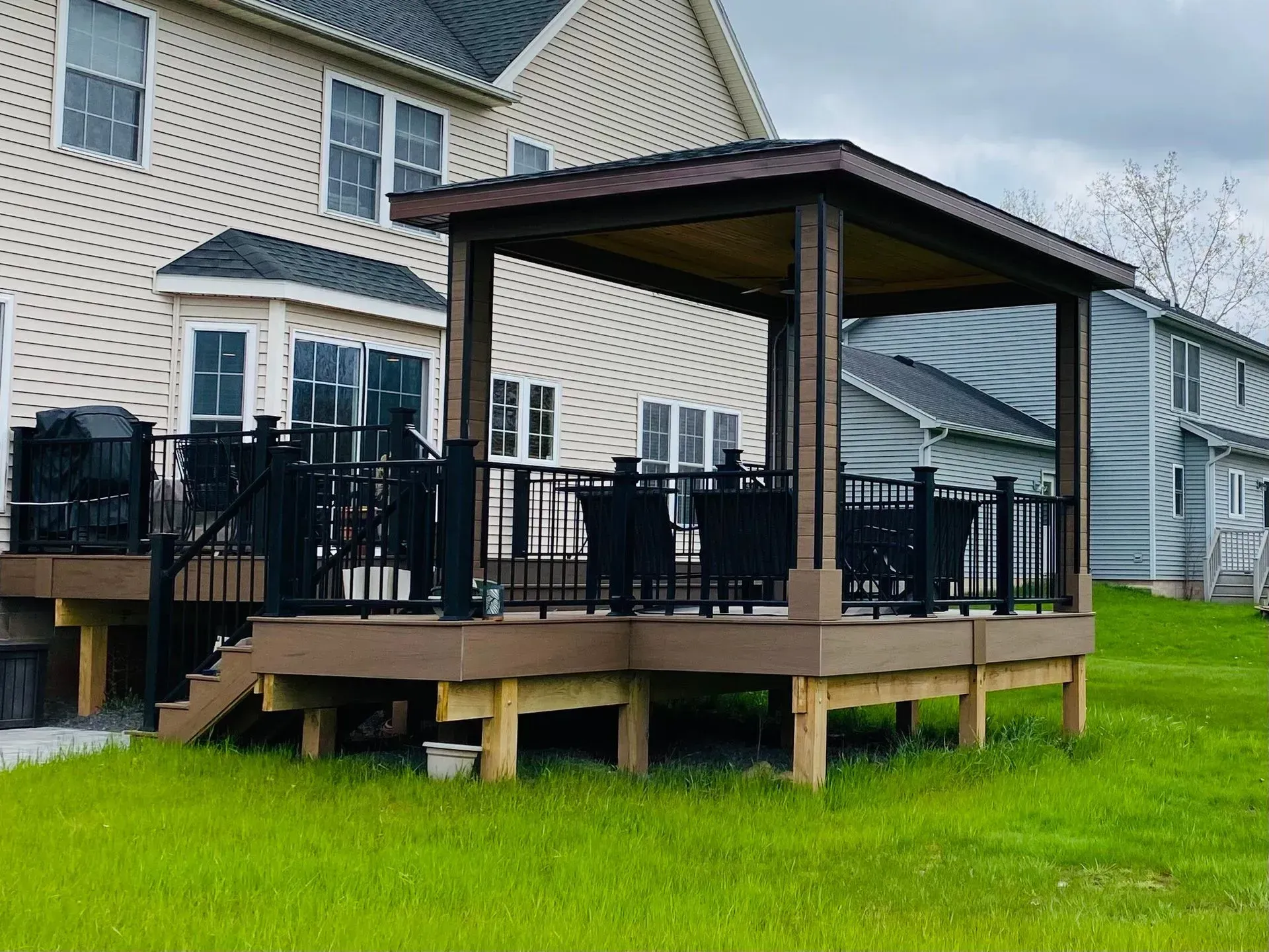 A deck with a gazebo on top of it in front of a house.