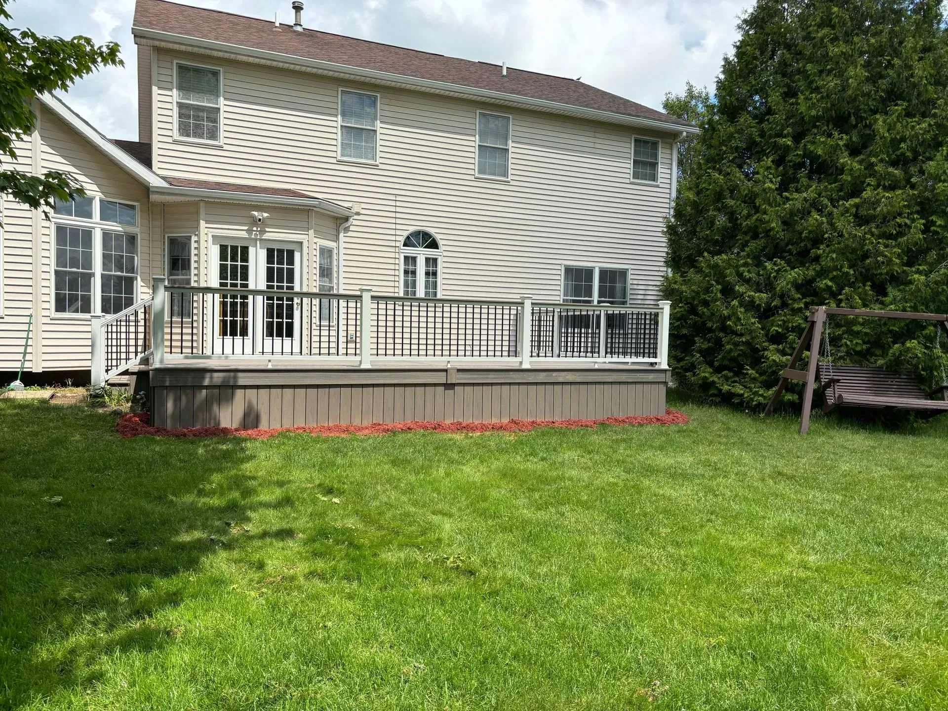The backyard of a house with a large deck and a swing.