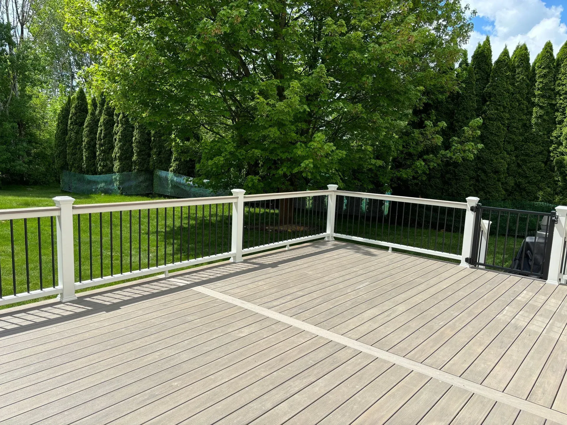 A large wooden deck with a white railing and trees in the background.
