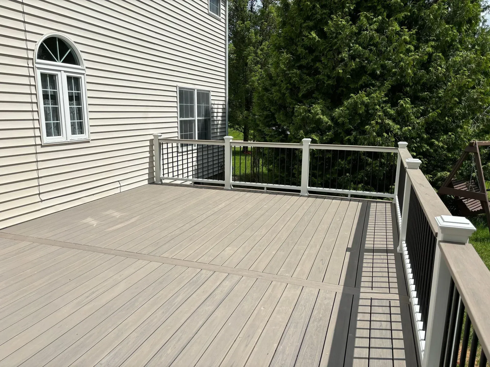 A large gray deck with a white railing is in front of a house.