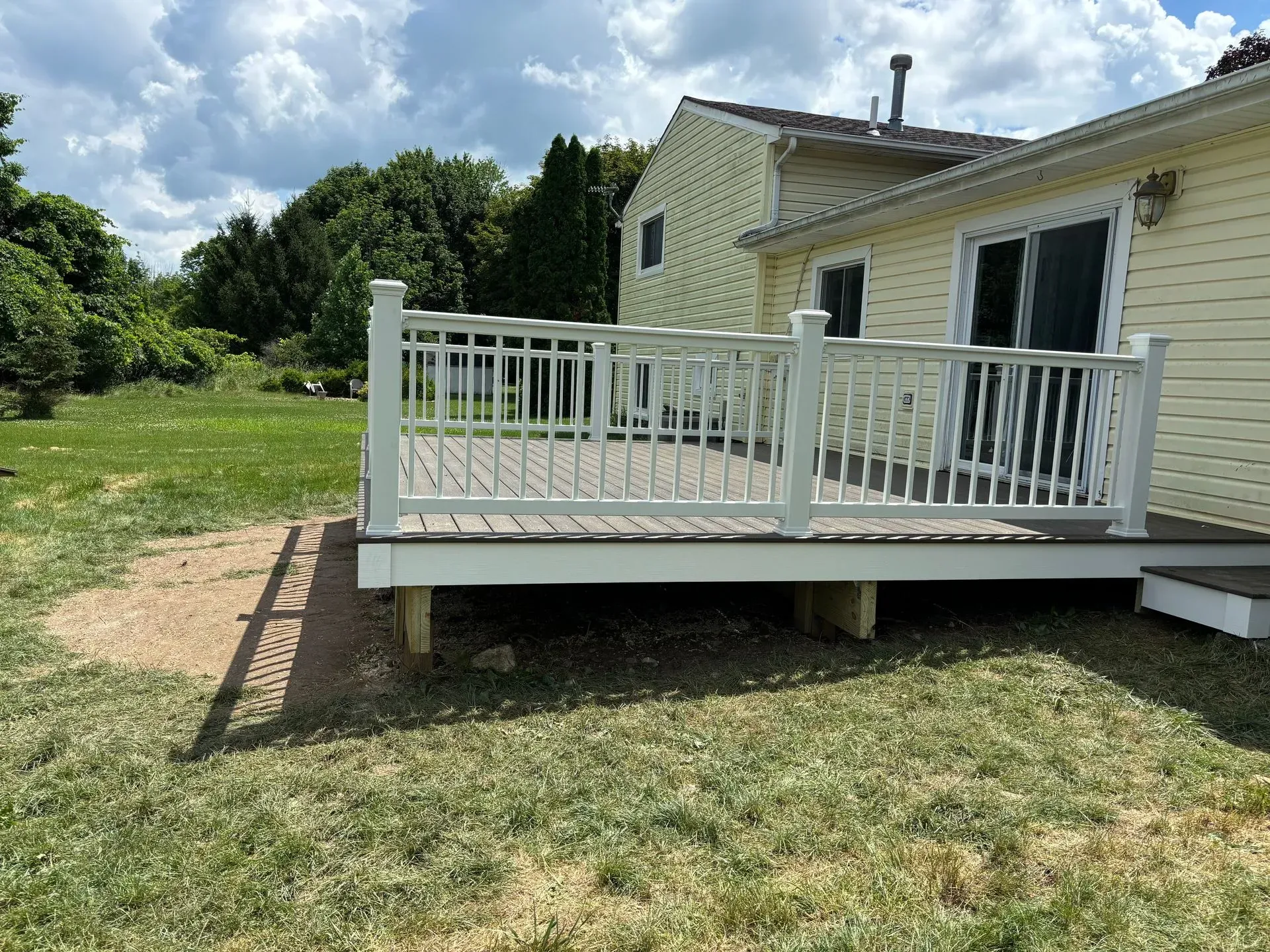 A large deck with a white railing is in the backyard of a house.