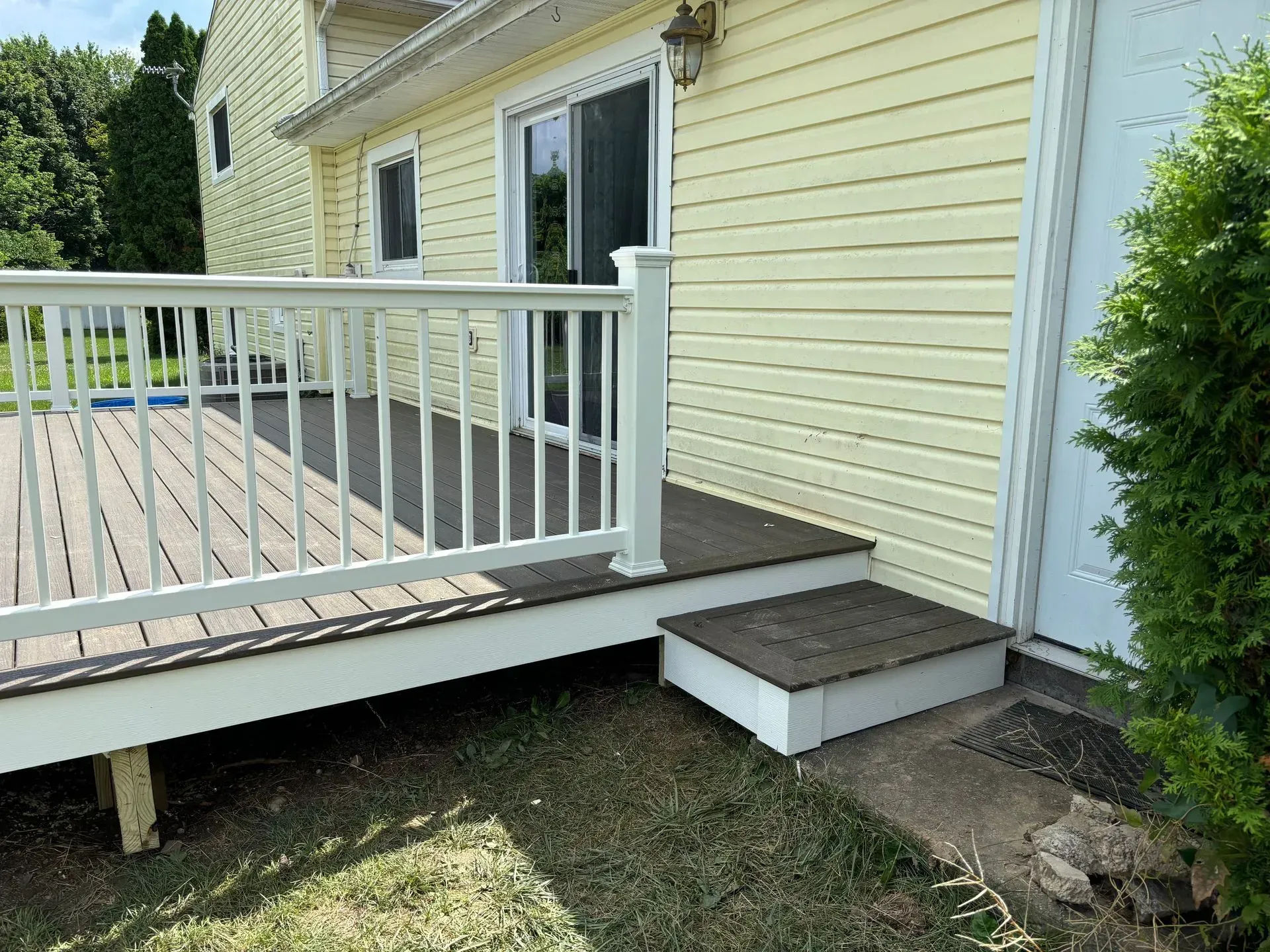 A wooden deck with a white railing is in front of a yellow house.