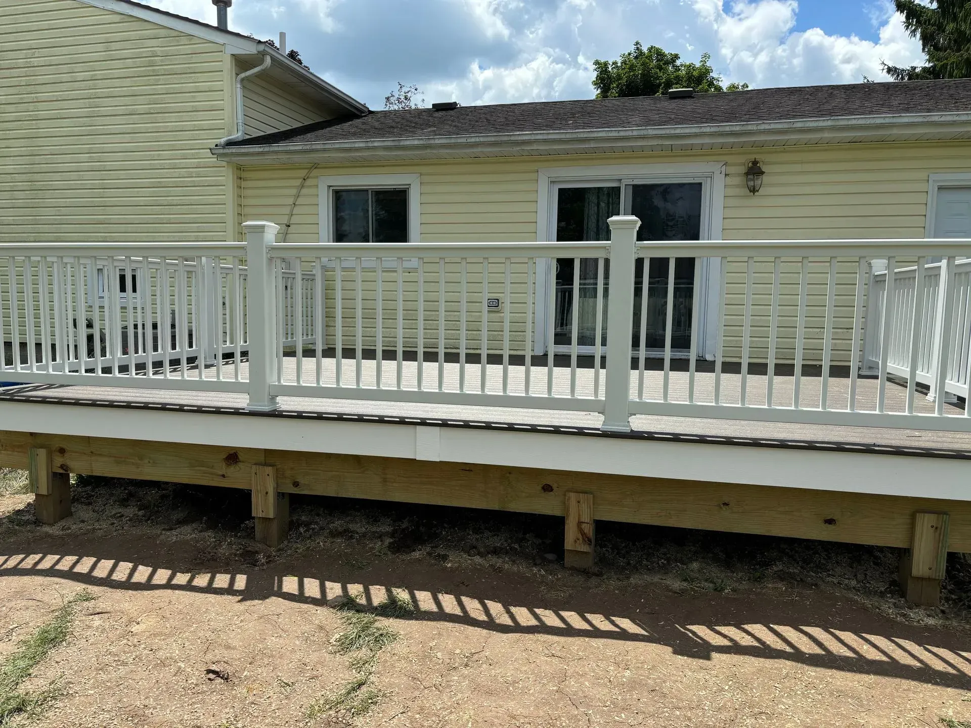 A deck with a white railing is in front of a house.