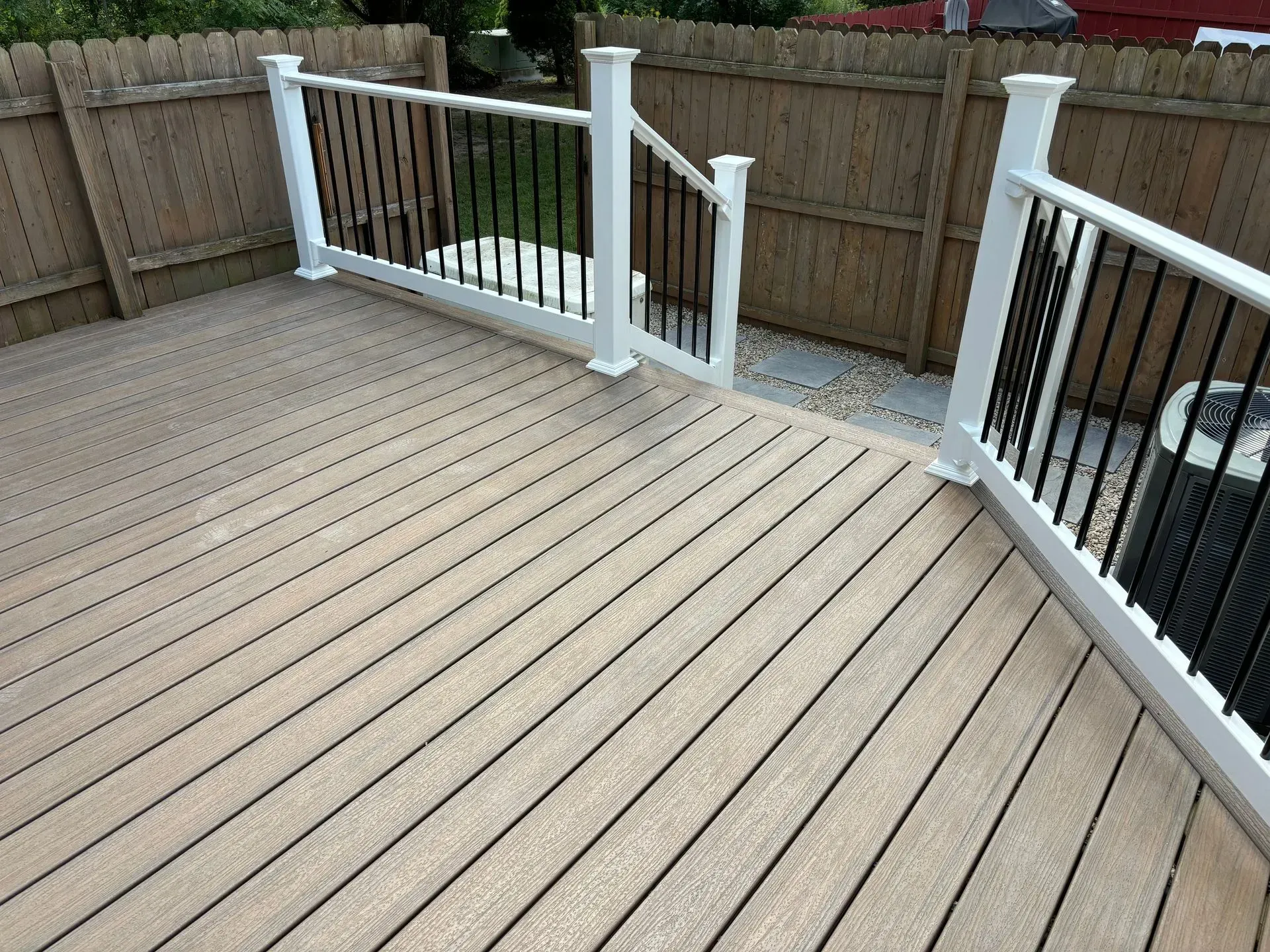 A wooden deck with a white railing and a wooden fence behind it.