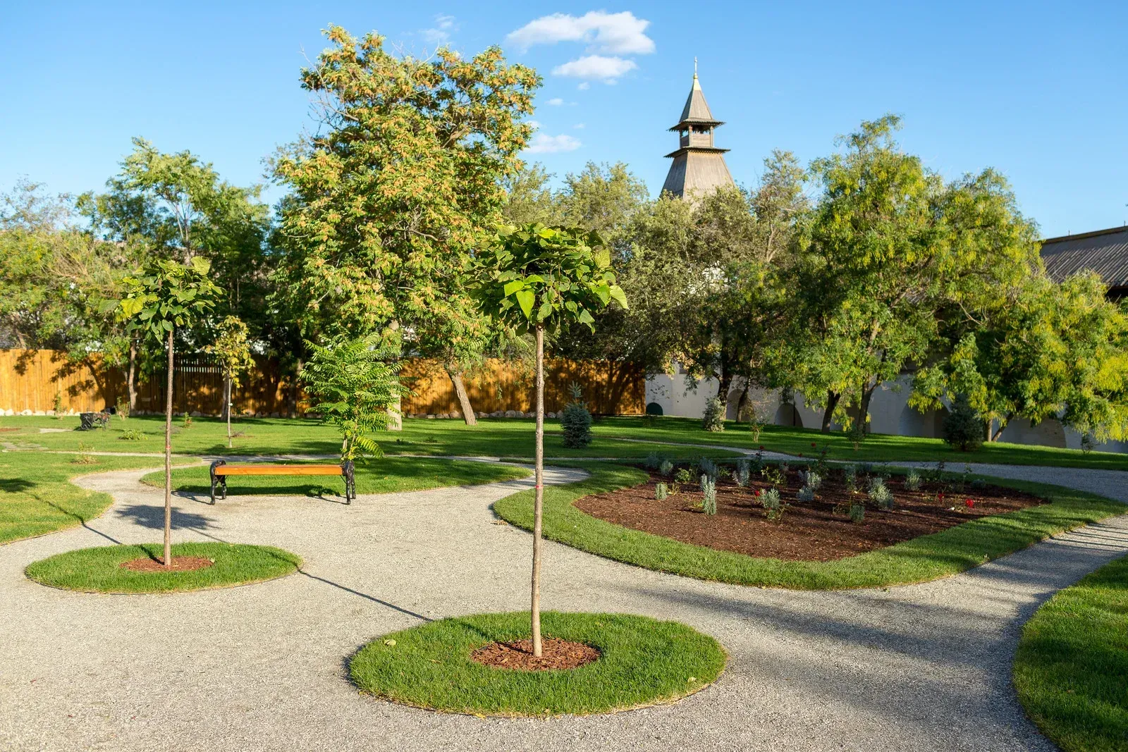 A park with a bench and trees and a church in the background.