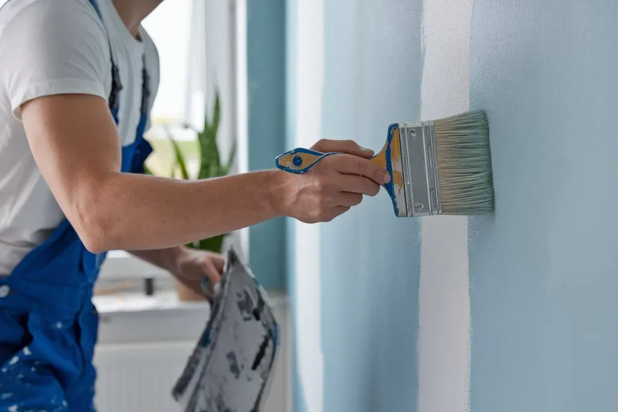 Person in blue overalls painting a light blue wall with a paintbrush
