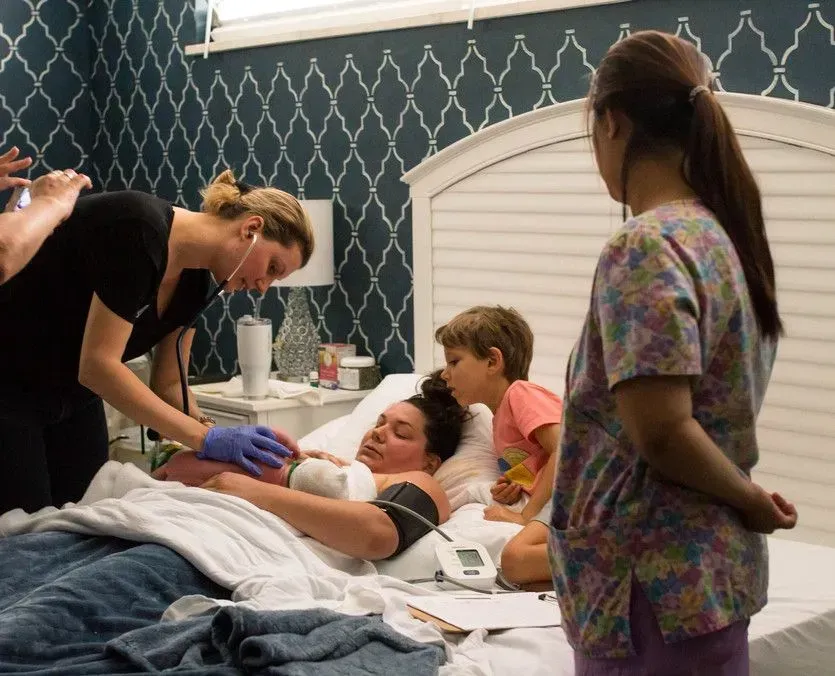 Woman giving birth in bed with medical staff and children present.