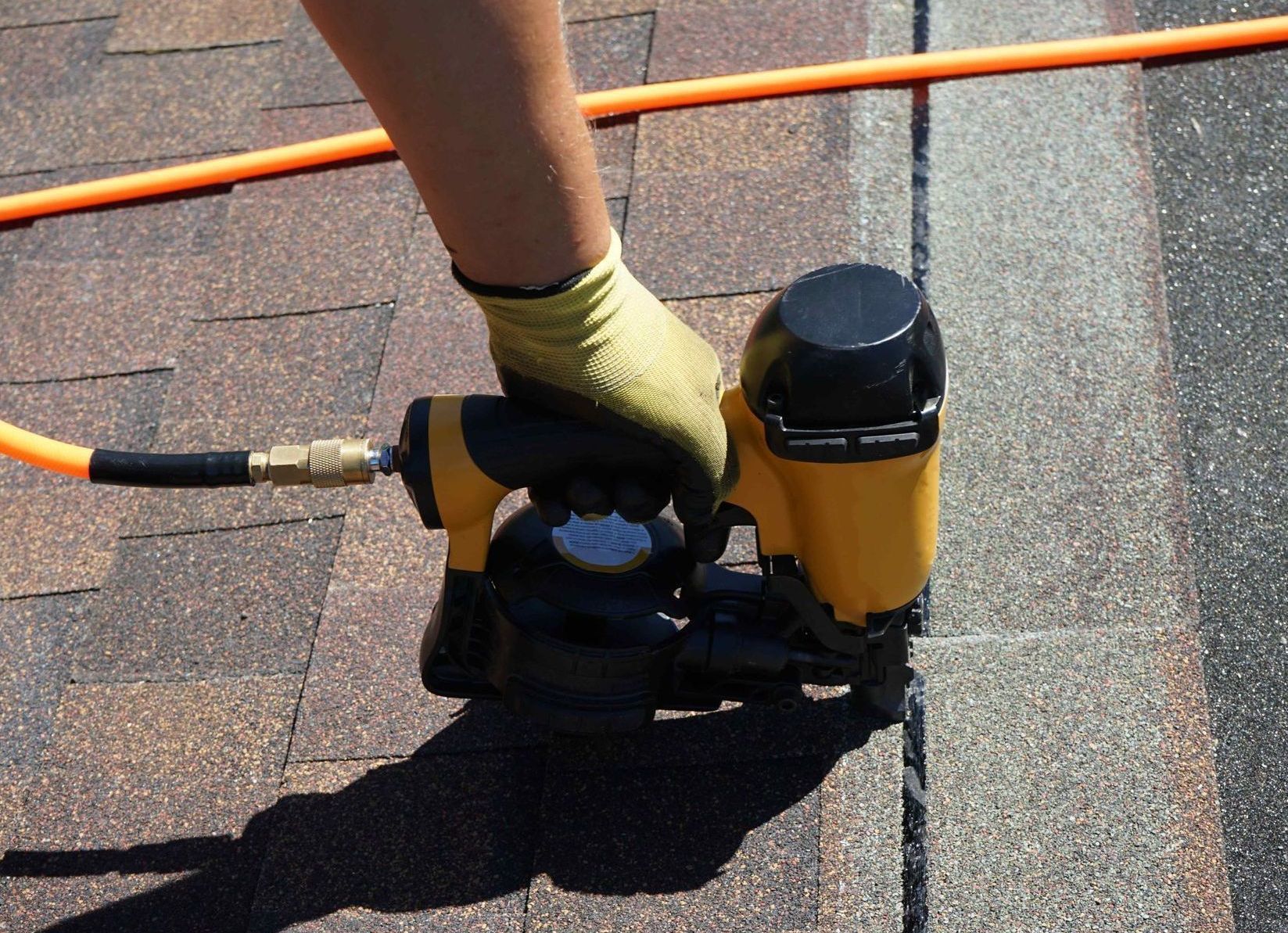 close up of a nail gun installing asphalt shingle roof 