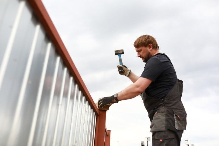 Man hammering a piece of metal on a roof with a cloudy sky.