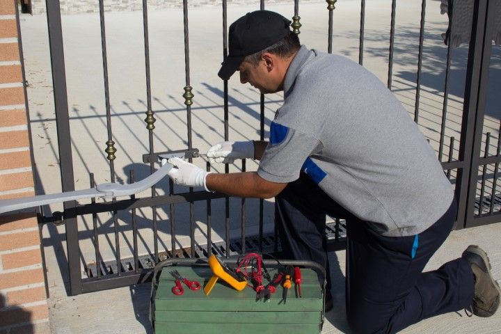 Person in gray uniform kneels, working on a metal gate with tools.
