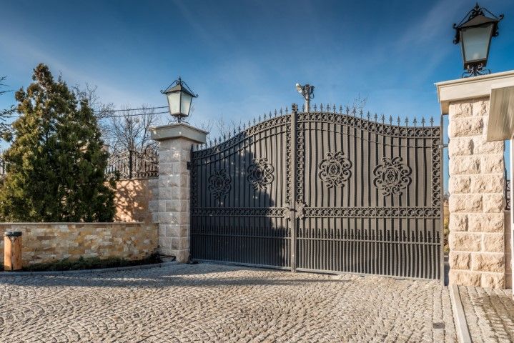 Ornate black metal gate with stone pillars under a blue sky.