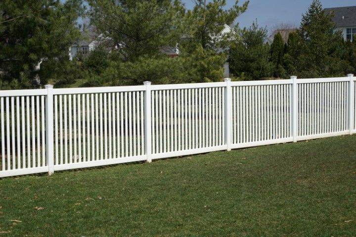 White picket fence on a green lawn, trees and houses in the background.