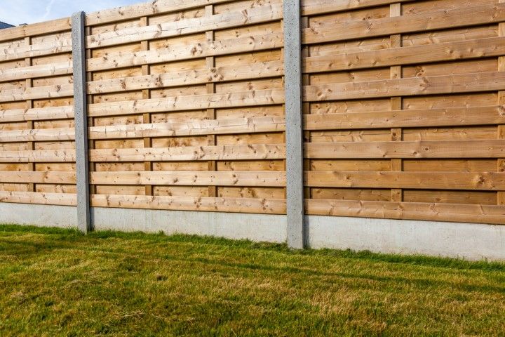 Wooden fence with concrete posts and a patch of green grass.
