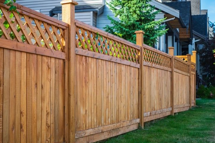 Wooden fence with lattice top, surrounding a green lawn next to a building.