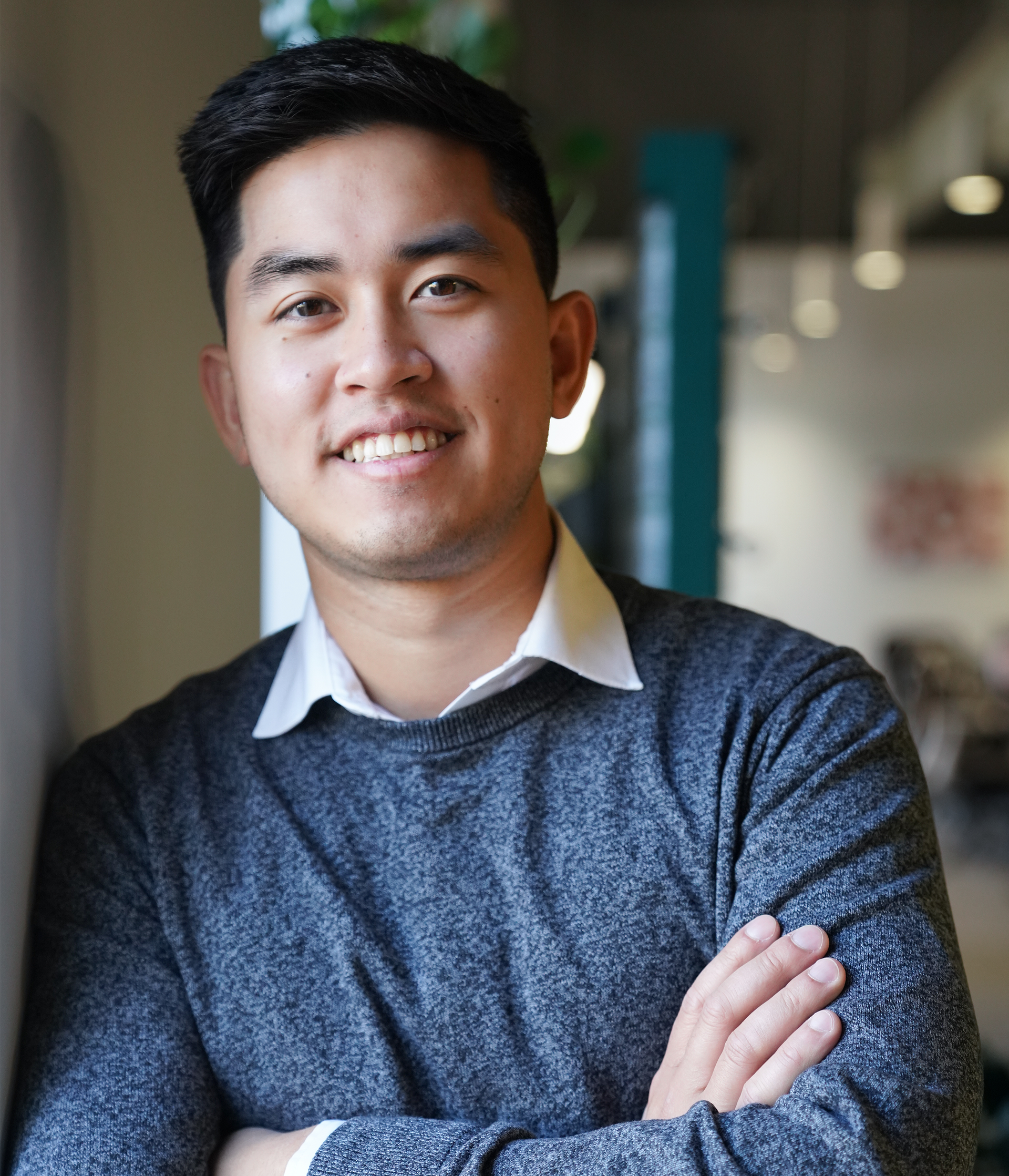 A man in a grey sweater is smiling with his arms crossed.