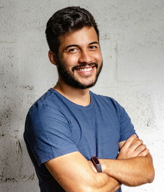 A man with a beard is standing with his arms crossed and smiling.