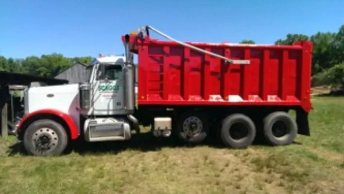 A white and red dump truck is parked in a grassy field