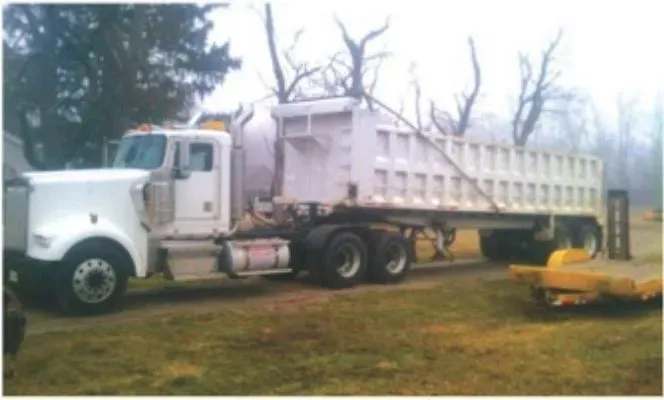 A white dump truck is parked in a grassy field