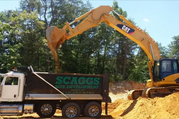 A cat excavator is loading dirt into a scaogs dump truck