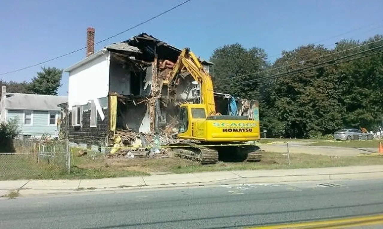 A yellow excavator is demolishing a house on the side of the road in Southern MD.